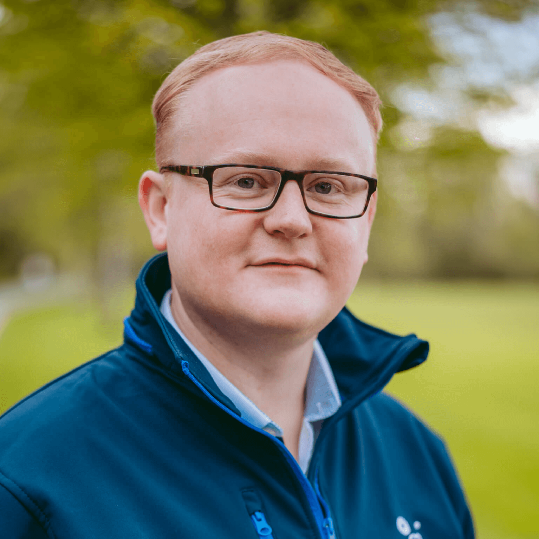 Killian wearing a dark blue jacket. Killian is looking happy directly into the camera. He is wearing black-framed eyeglasses.
